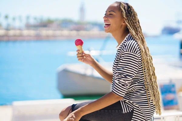 Zwarte vrouw die een aardbeienijs eet terwijl ze geniet van het uitzicht op de zeehaven. — Stockfoto