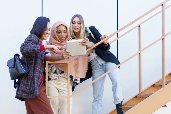 Sorrindo jovens senhoras diversas usando tablet nas escadas — Fotografia de Stock