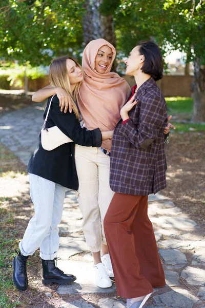 Deleitado jóvenes diversas mujeres abrazando y sonriendo en el parque —  Fotos de Stock