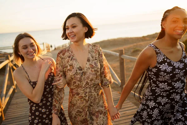 Мультиэтнические девушки, гуляющие по пешеходному мосту на берегу моря — стоковое фото
