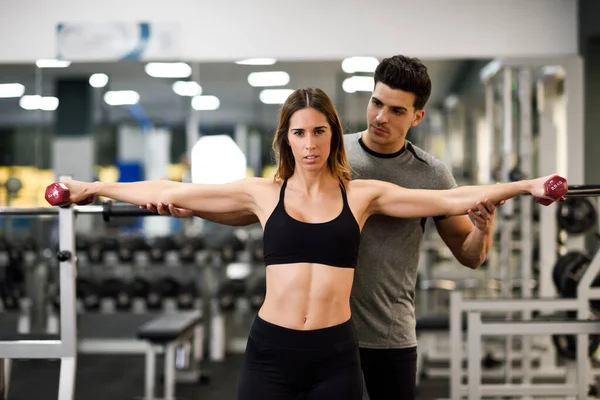 Entrenador personal ayudando a una joven a levantar pesas — Foto de Stock