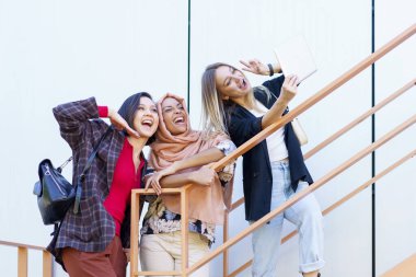 Heyecanlı genç çok ırklı kadın milenyumlar gülümsüyor ve tabletten selfie çekiyor.