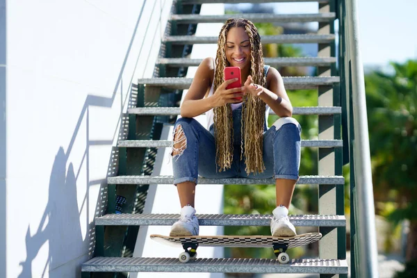 Vrolijke zwarte vrouwelijke skater browsen smartphone in de stad — Stockfoto