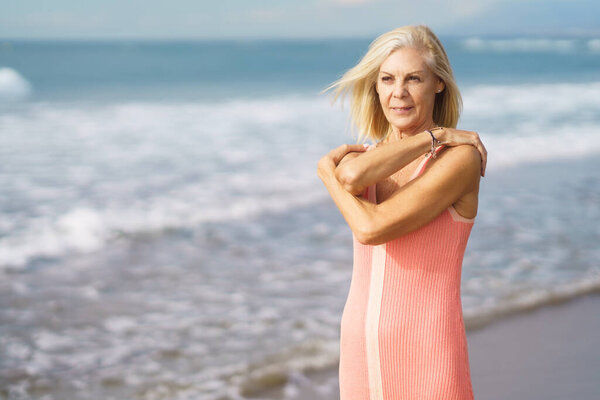 Mature woman enjoying her free time looking at the sea from the shore of the beach.