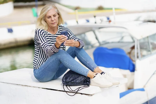 海の港に座っているスマートフォンを使って熟女. — ストック写真