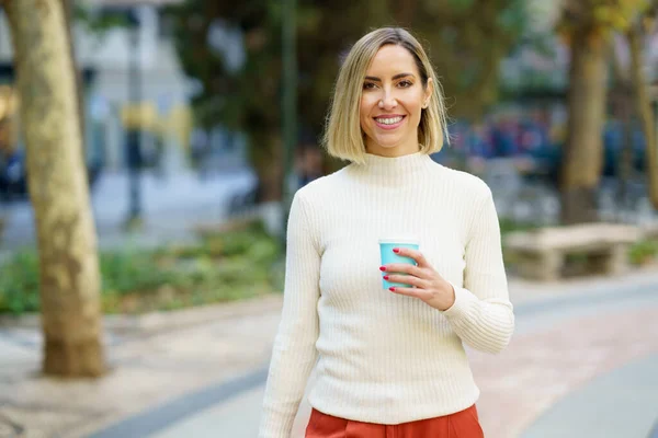Donna sorridente con tazza di bevanda in piedi sulla strada — Foto Stock
