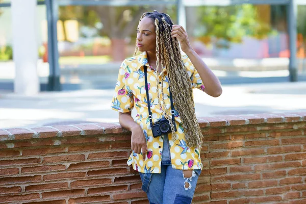 African influencer combed with colorful braids standing with a camera outdoors. — ストック写真