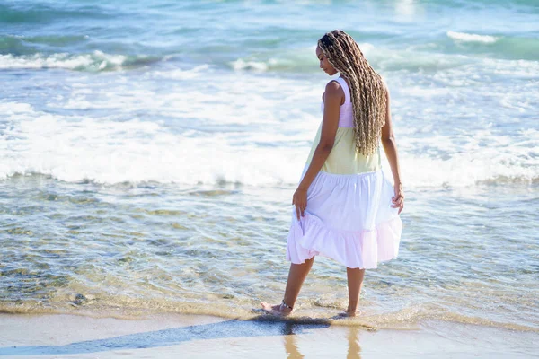 Black female walking along the shore of the beach wearing a beautiful long dress. — Stock Photo, Image