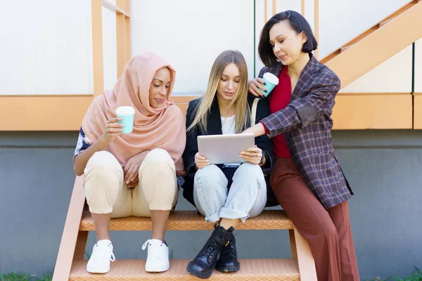 Stylische Freundinnen teilen Tabletten und trinken Kaffee zum Mitnehmen auf der Straße — Stockfoto