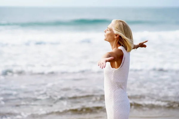 Зрелая женщина раскрывает руки на пляже, проводит досуг, наслаждаясь свободным временем — стоковое фото