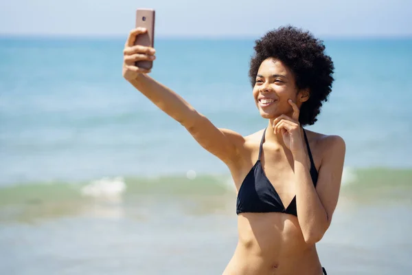 Afro saçlı Afro-Amerikalı bir kadın tropik bir plajda akıllı telefonuyla selfie çekiyor.. — Stok fotoğraf