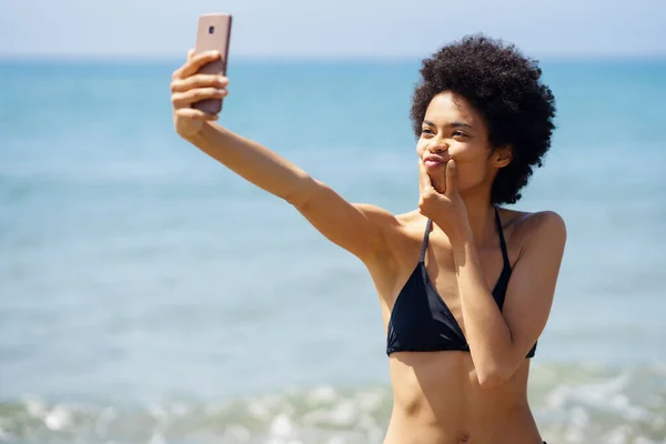 Mulher negra com penteado afro tirar uma selfie com um gesto engraçado em uma praia tropical. — Fotografia de Stock