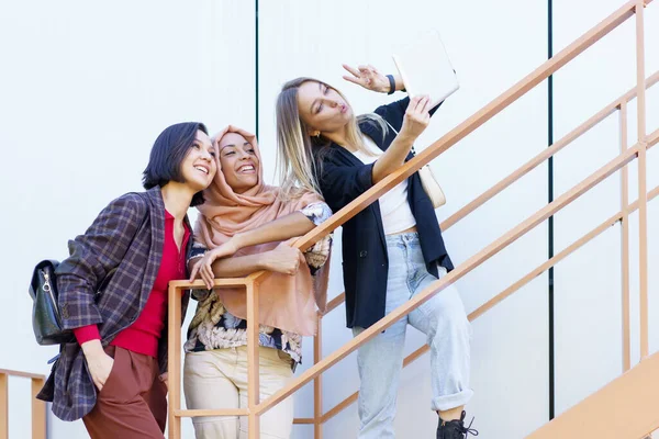 Emocionados jóvenes milenarias multiétnicas sonriendo y tomando selfie en la tableta —  Fotos de Stock