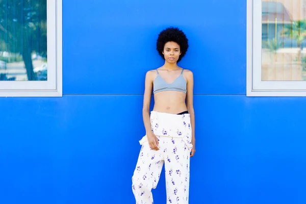穿着长裤和胸罩 靠着城市蓝墙摆姿势的黑头发年轻女人 时装模特 — 图库照片
