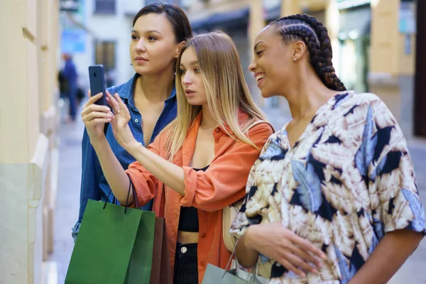 ショッピングバッグを持つ多様な女性の友人のグループは ショッピング中に路上で商品を選択しながら携帯電話でショーケースを撮影 — ストック写真