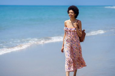 Sırt çantasıyla sahilde dalgalanan tropikal denizin yanında duran ve yaz tatilinde seyahat ederken gözlerini kaçıran genç etnik kadın.