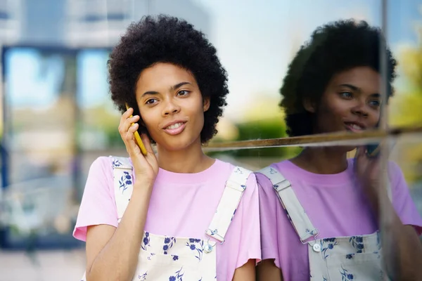 陽気なアフリカ系アメリカ人の女性は カジュアルな服を着てスマートフォンで話して笑っています 都会の中で幸せな若い女性 — ストック写真