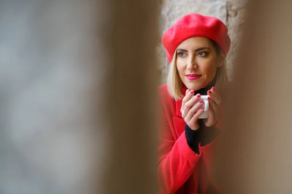 透过那模糊的红色贝雷帽迷人的女性 手握一杯咖啡 凝视着远方 — 图库照片