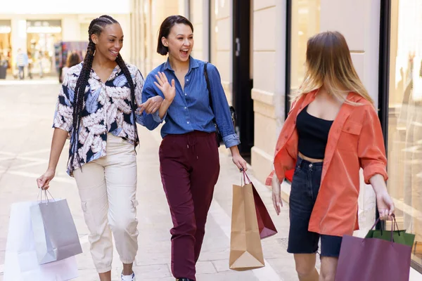 在城市购物后 一些持购物袋互相望着 边走边打招呼的多种族女性朋友走在大楼附近的街上 — 图库照片