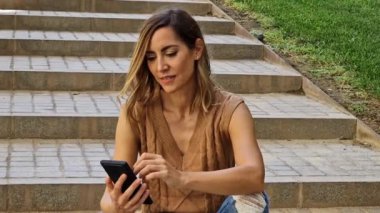 Açık havada orta yaşlı bir kadın akıllı telefonunu bir kalem ya da stil ile kullanıyor. Kafkasyalı kadın günlük kıyafetler giyiyor..