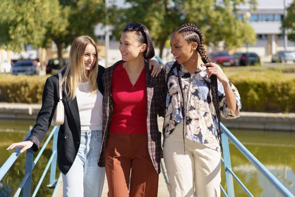コンテンツのグループ緑豊かな都市の晴れた夏の日に川を渡る歩道橋を歩く多様な女性の友人 — ストック写真