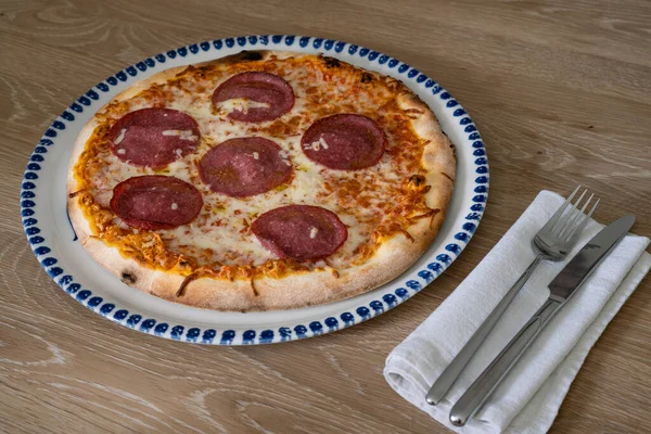Salami Pizza Italian Style on a Round Plate with Knife and Fork
