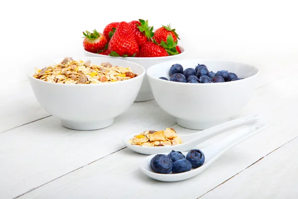 Färska blåbär, jordgubb och cornflakes i vita Porslinsskålar, träbord — Stockfoto