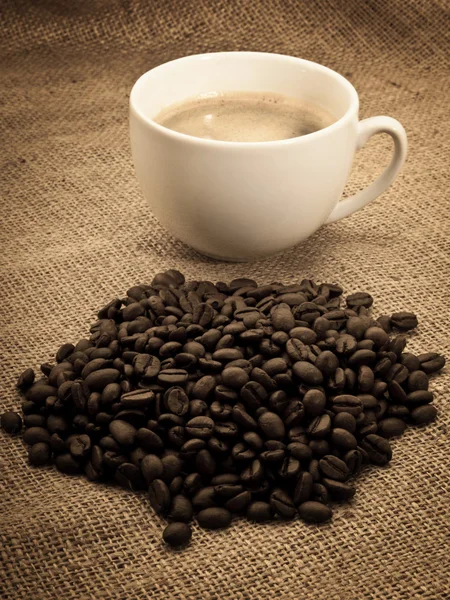 Кавові зерна з чашкою кави на мішку тканини — стокове фото