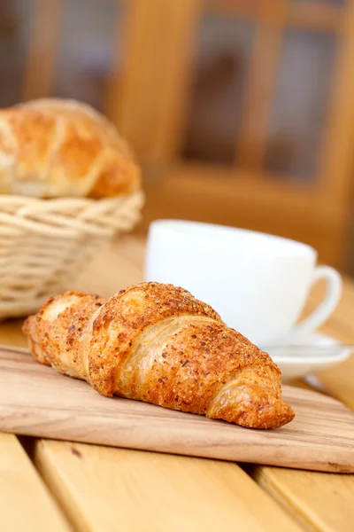 Friss croissant-t és a fehér csésze kávé, egy fából készült asztal — Stock Fotó