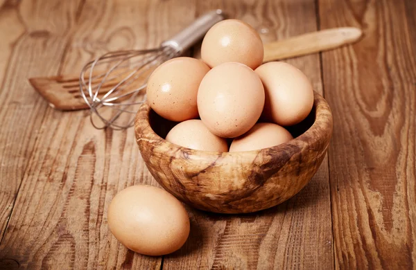 Frische braune Eier mit Schneebesen auf Holzgrund — Stockfoto