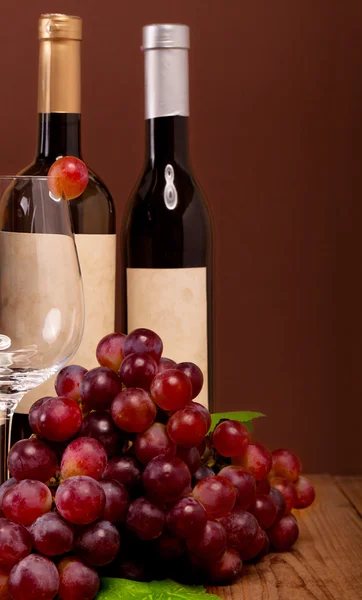 Uvas rojas con botellas de vino sobre fondo marrón —  Fotos de Stock