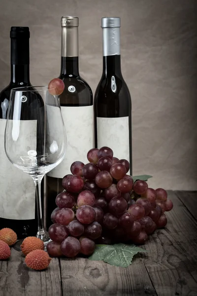 Uvas rojas con botellas de vino sobre fondo de madera —  Fotos de Stock