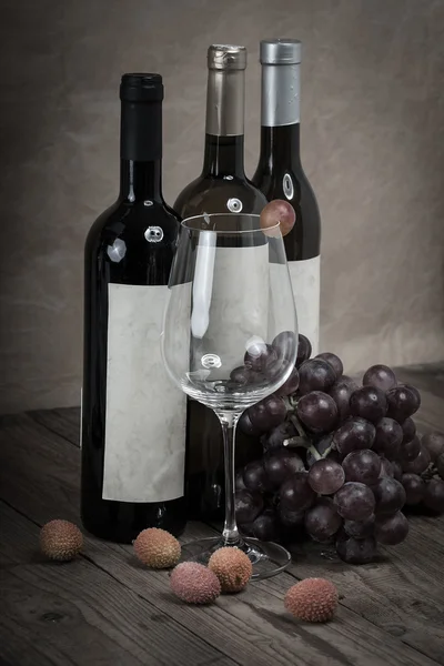 Röda druvor med vinflaskor på trä bakgrund — Stockfoto