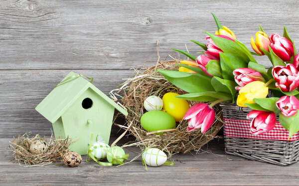 easter decoration with eggs, birdhouse and tulips. wooden backgr