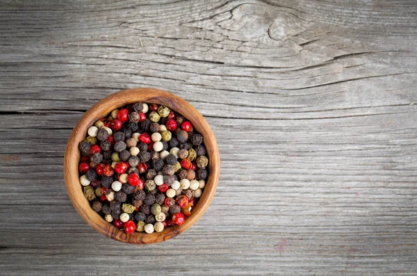 Poivre coloré dans le bol en bois, sur une planche en bois — Photo