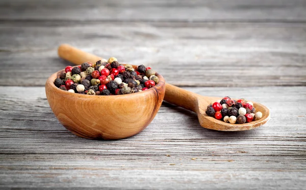 Gekleurde peper in de houten kom, op houten bord — Stockfoto