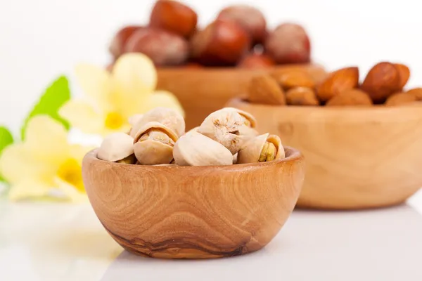 Pistacho, almendras, avellanas con flores en el cuenco de madera . — Foto de Stock