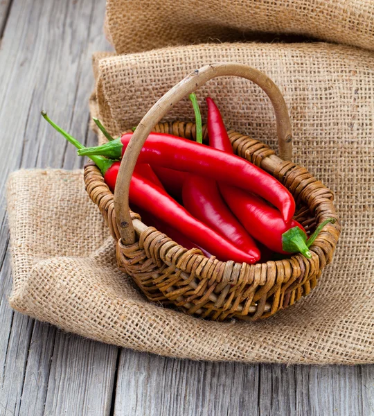 Red chili pepper in a wicker basket with burlap on the wooden ba — Stock Photo, Image