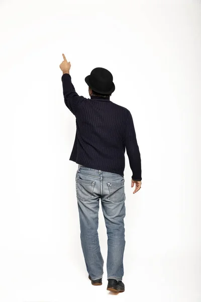 后面的人走的时候用手指指示一个向上的点 他穿着一件蓝色毛衣 牛仔裤和一顶圆顶礼帽 因白人背景而被隔离 — 图库照片