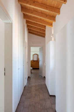 Yan taraflarında beyaz duvarlar ve kapılar olan koridorun önü. Dipte aynalı açık bir kapı var. İçeride kimse yok.