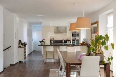 Deri masa ve sandalyeli açık alan ve arka planda tabureler olan modern bir mutfak. Modern daire. İçeride kimse yok.