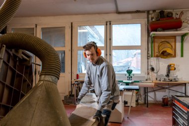 Genç bir marangozun stüdyo portresi dairesel bir testereyle odun keserken. Kırmızı zemin ile büyük boşluk.