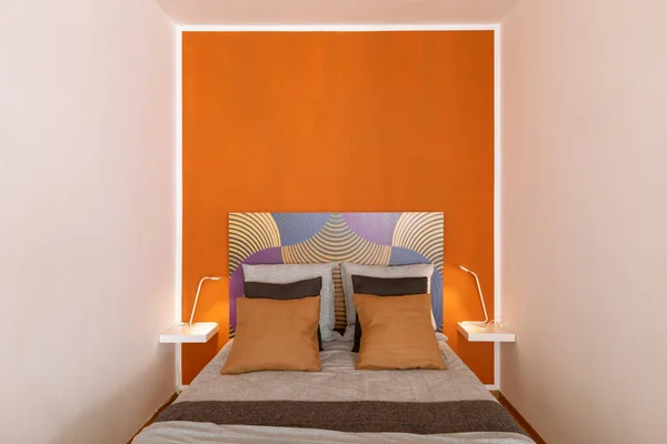 枕がたくさんある毛布とベッドのフロントビューとベッドサイドテーブルにはランプがあります オレンジと白の壁 — ストック写真