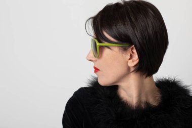 Beyaz arka planda siyah giyinmiş zarif bir kadının portresi. Agresif ve kışkırtıcı bir profil. Yeşil güneş gözlüğü var..