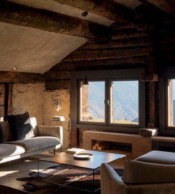 Dağ evi oturma odası, büyük bir kanepe, iki koltuk ve Alplere bakan büyük bir pencere. Tahta kirişler ve içinde kimse yok.