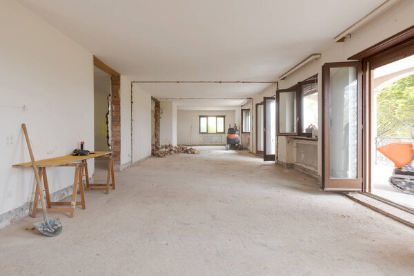 Large bright room with many windows of an old villa undergoing demolition and renovation. The walls have been knocked down and the floor is gone. Nobody inside
