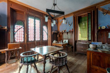 Ahşap masa ve koltuklu yemek odası, duvarda mavi döşeme ve duvarda geyik boynuzları asılı duvar. Terk edilmiş bir villanın içi restore edilecek.