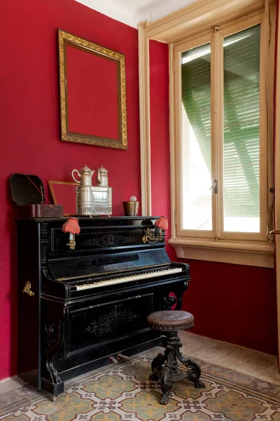 スツールとシャッター窓の黒いピアノの詳細 壁には大きな枠がかかっている 放棄された別荘の内装を復元する — ストック写真