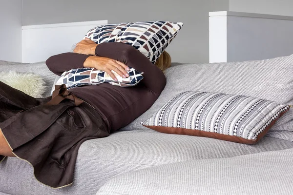 Charming middle-aged woman sitting on the sofa at home with a pillow on her face. She is depressed and lonely. Copy-space