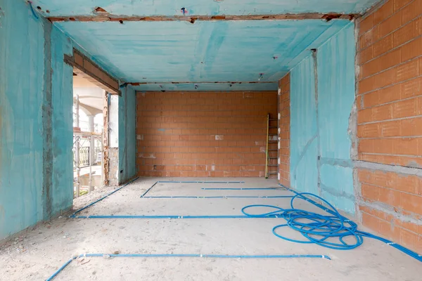 Interior of an ancient villa under renovation with blue painted walls, electrical pipes on the ground and freshly laid orange bricks. Nobody inside